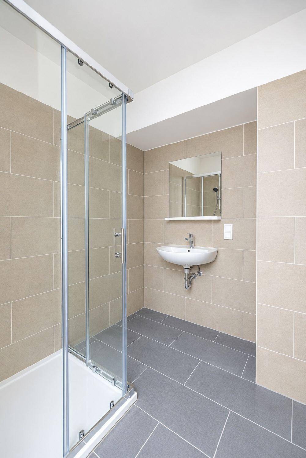 Modernes Badezimmer mit beigefarbenen Wandfliesen, grauen Bodenfliesen und einer Duschkabine.