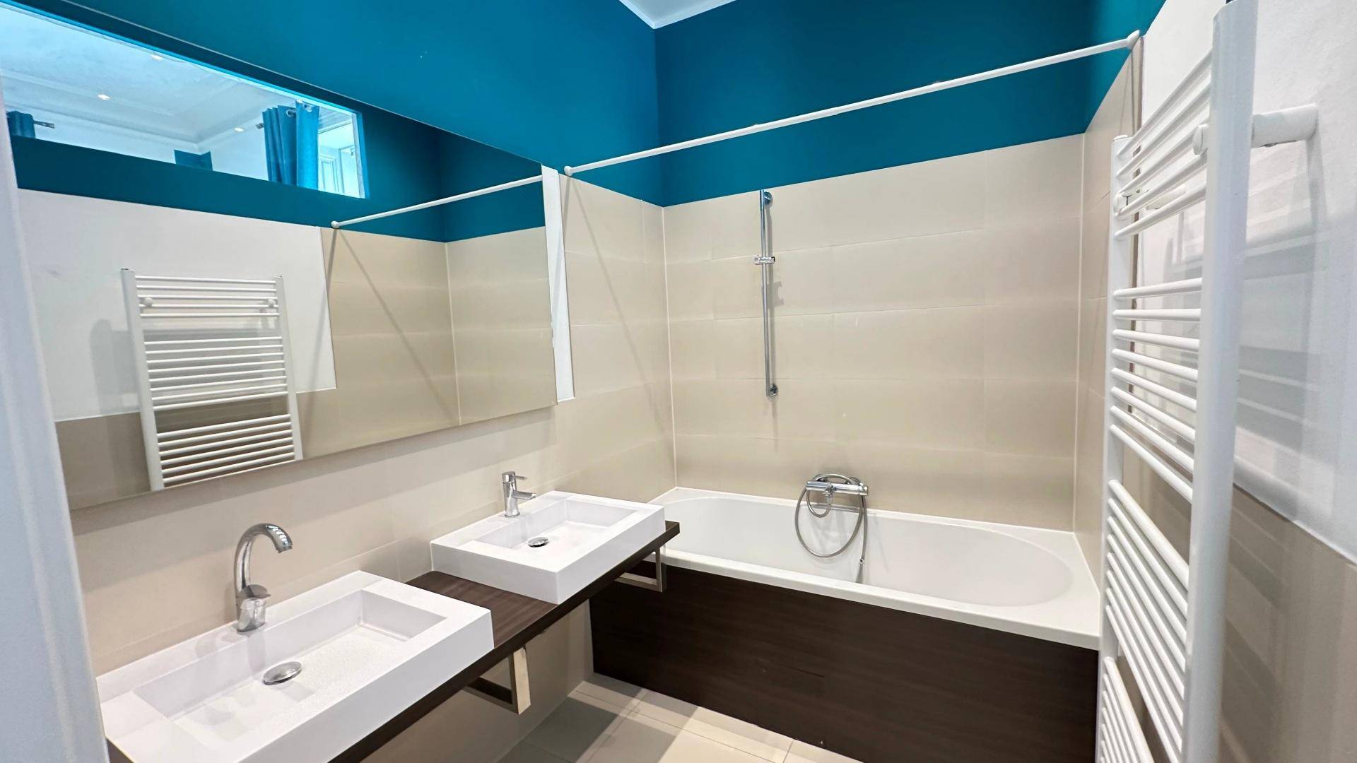 Modernes Badezimmer mit Doppelwaschbecken, Badewanne und blauer Decke.