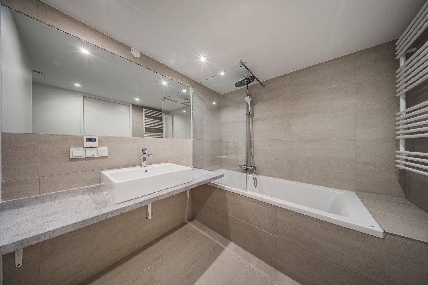 Modernes Badezimmer mit Badewanne, Regendusche, großem Spiegel und beheiztem Handtuchhalter.