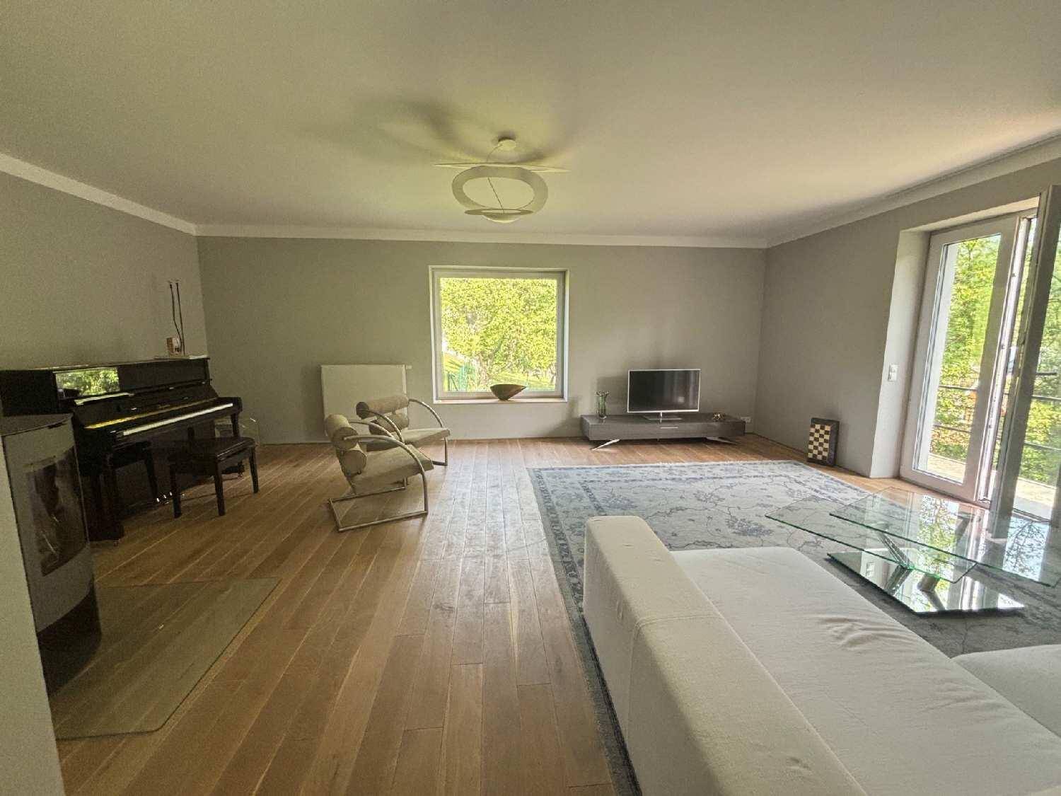 Geräumiges Wohnzimmer mit Holzboden, Klavier und Blick ins Grüne durch große Fenster.