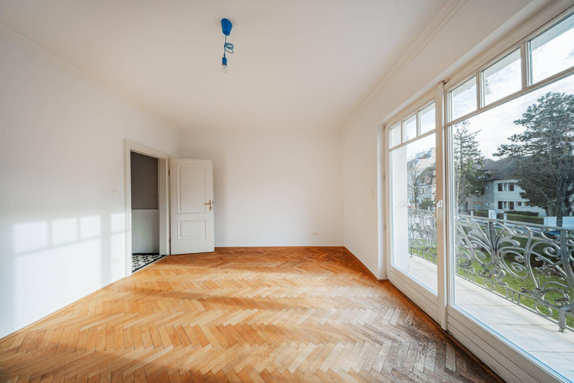 Geräumiges Wohnzimmer mit Fischgrätparkett und Zugang zu einem großen Balkon mit Ausblick.