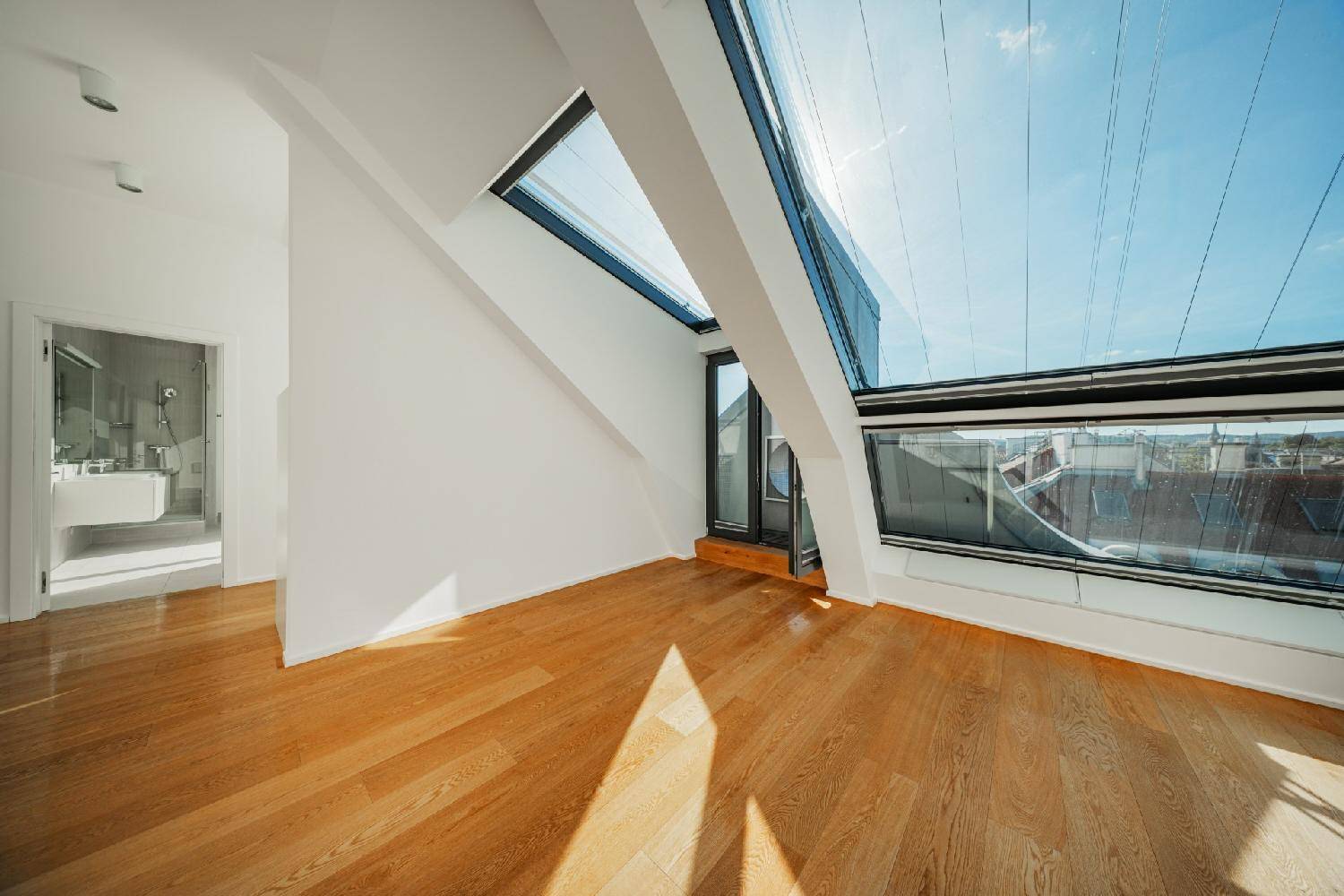 Lichtdurchfluteter Raum mit Holzboden und schrägen Dachfenstern, die einen hellen und offenen Eindruck vermitteln.
