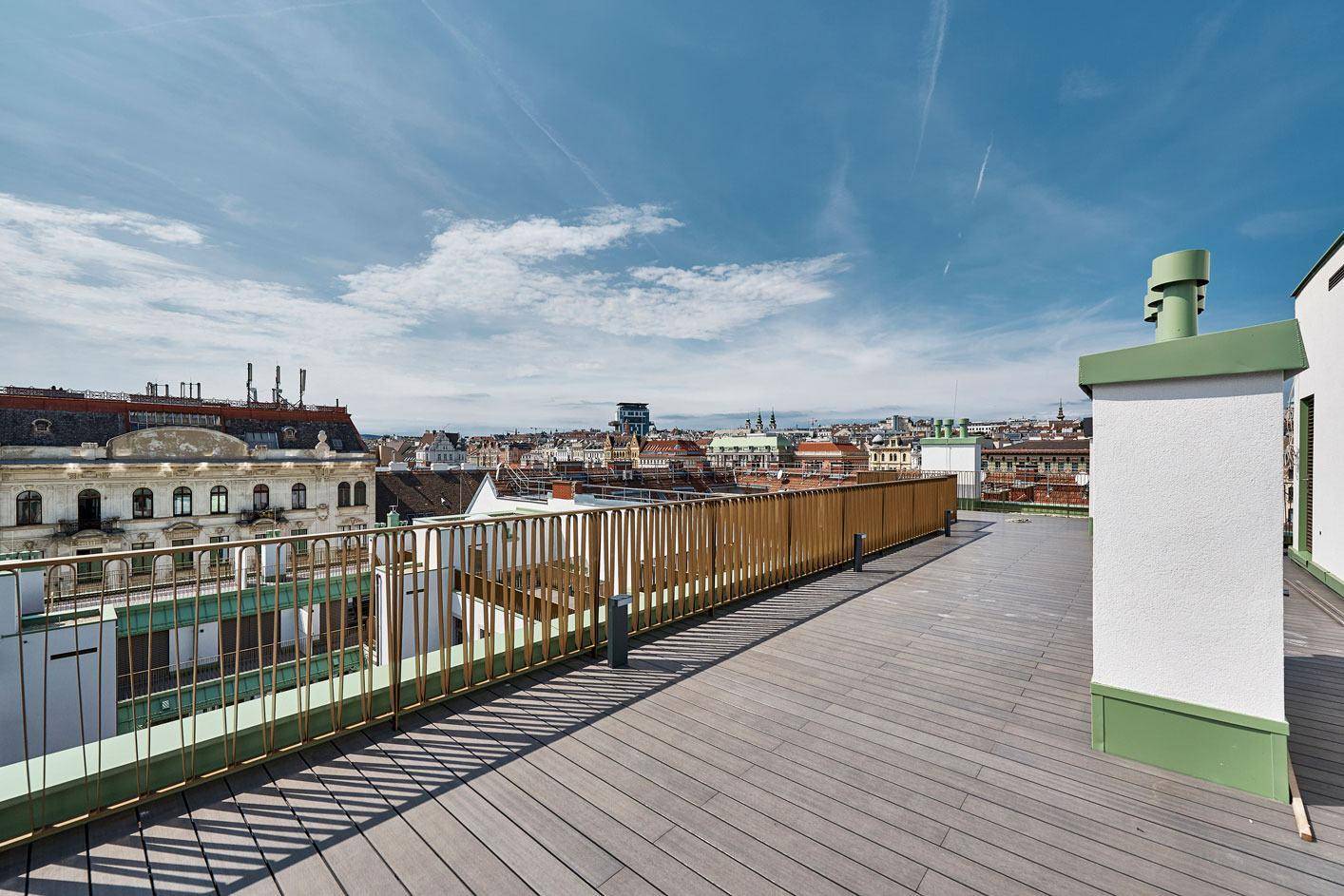 Weitläufige Dachterrasse mit Holzboden und Panoramablick über die Dächer der Stadt.