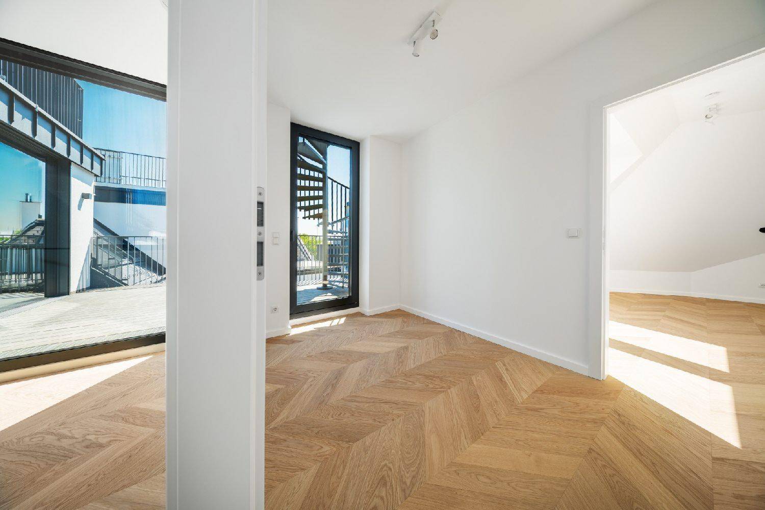 Kleiner Raum mit Fischgrätparkett und einer Wendeltreppe, die zu einem Außenbereich führt.