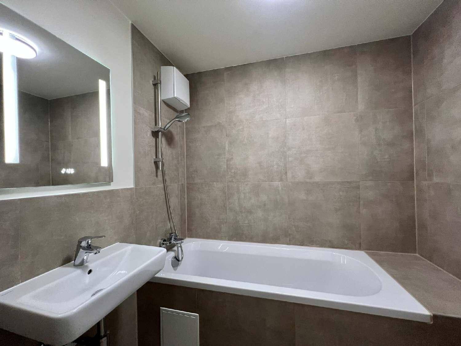 Modernes Badezimmer mit Badewanne, Duscharmatur und grauen Fliesen an den Wänden.