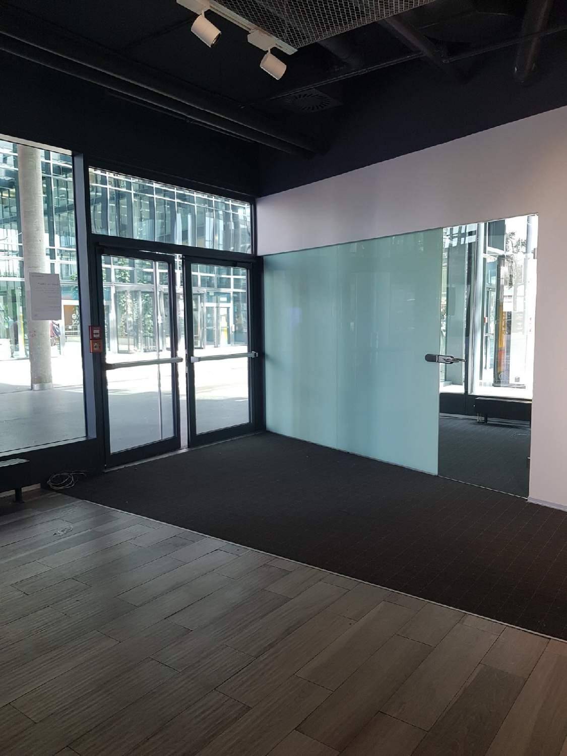 Eingangsbereich eines Gewerberaums mit großen Glasfronten und dunklem Teppichboden.