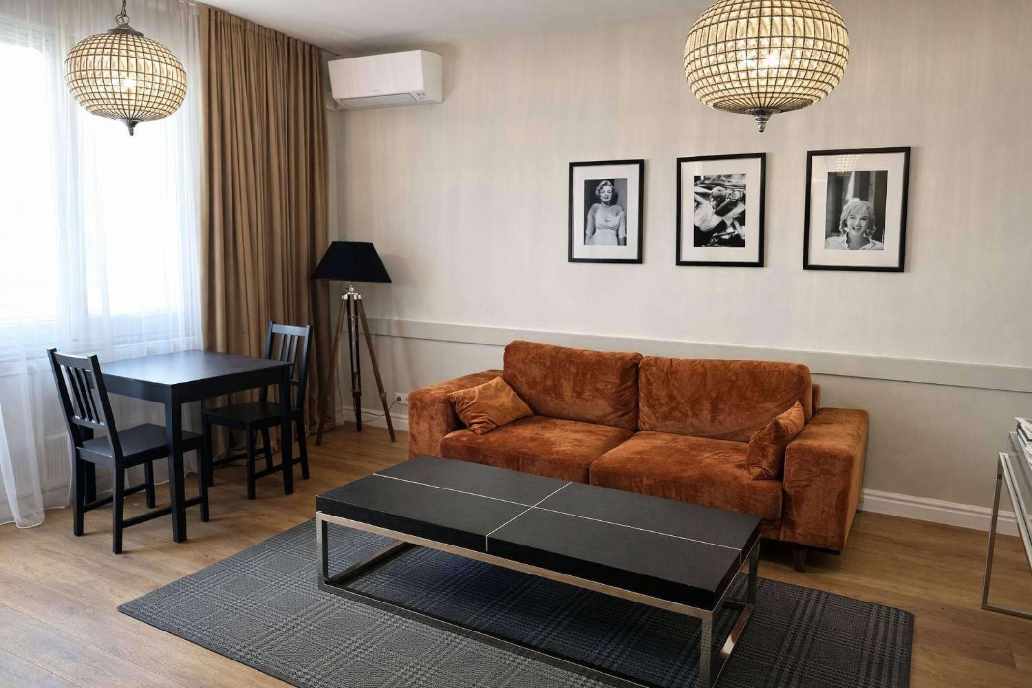 Gemütlicher Wohnbereich mit braunem Sofa, Esstisch und stilvollen Deckenleuchten.