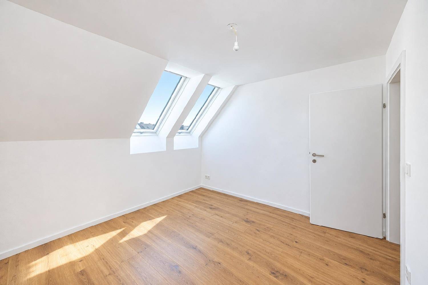 Helles Schlafzimmer im Dachgeschoss mit schrägen Wänden, Holzboden und zwei Dachfenstern.
