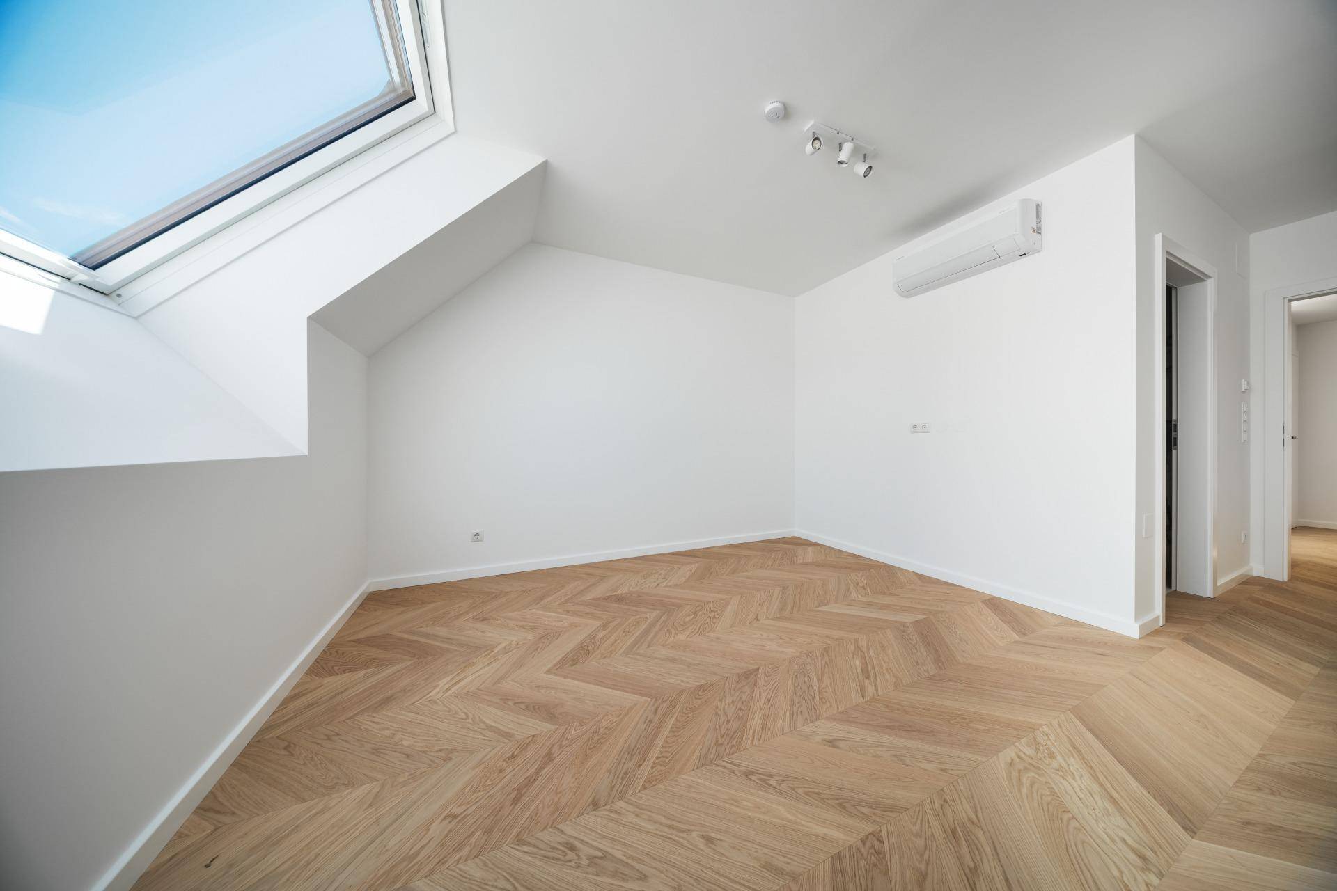 Helles Schlafzimmer mit Fischgrätparkett, Klimaanlage und einem Dachfenster für angenehmes Raumklima.