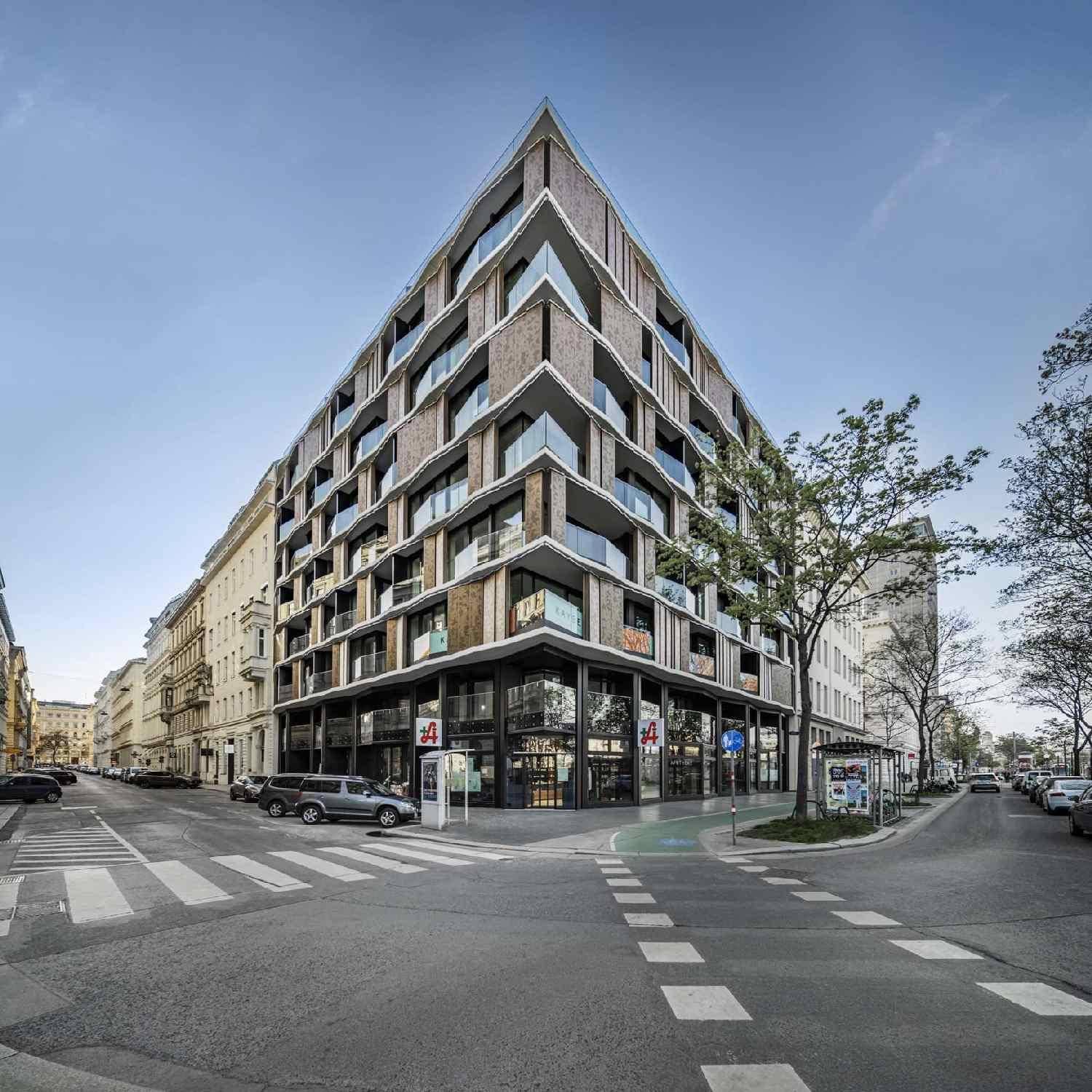 Modernes Eckgebäude mit markanter Architektur, großen Fenstern und Balkonen in urbaner Umgebung.