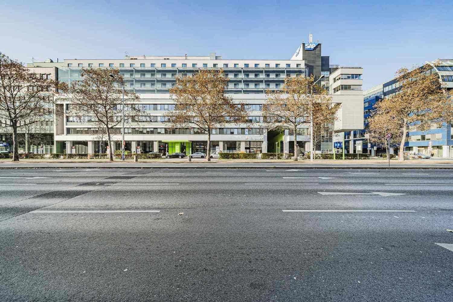 Modernes Bürogebäude mit vielen Fenstern und Bäumen an einer belebten Straße.