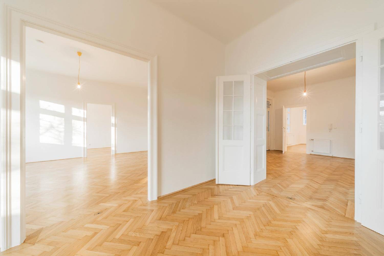 Heller Flur mit Fischgrätparkett und eleganten Doppeltüren, die zu weiteren Räumen führen.