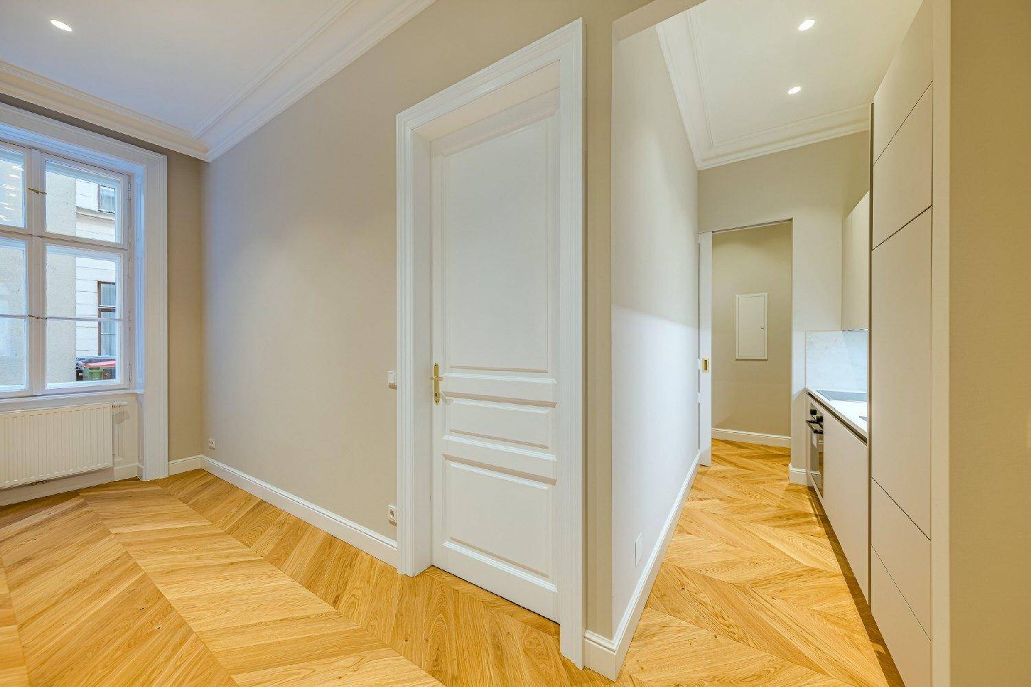 Heller Flur mit Fischgrätparkett, weißen Türen und Blick in eine moderne Küche und ein weiteres Zimmer.