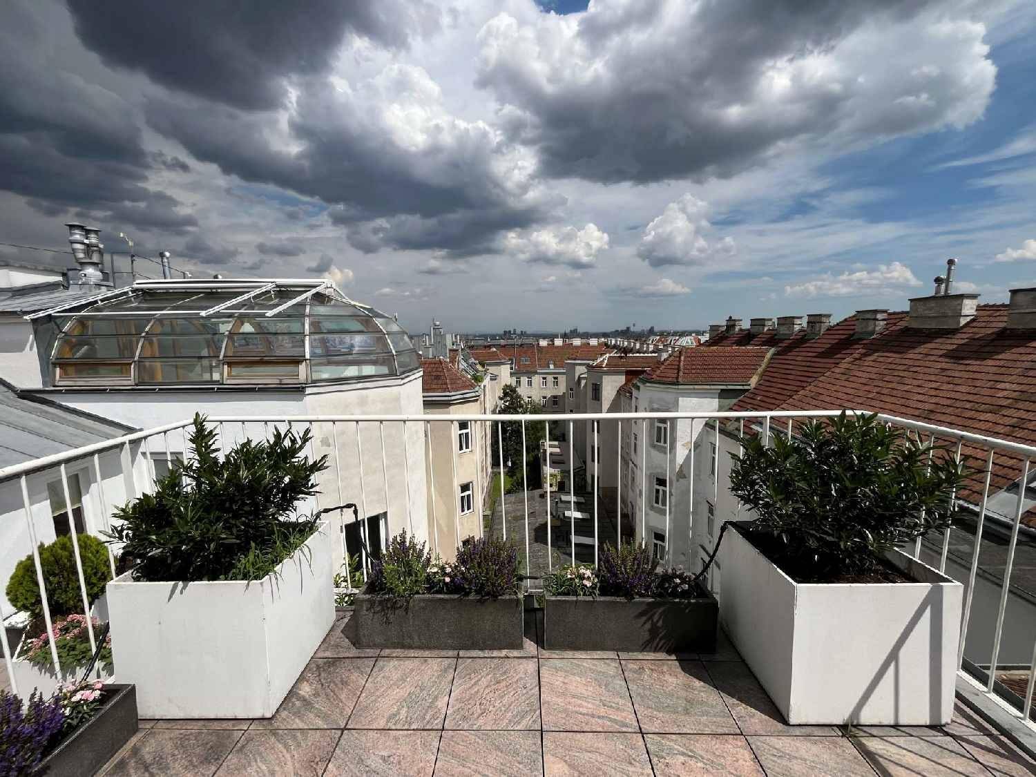 Geräumige Dachterrasse mit Fliesenboden, Pflanzen und weitem Blick über die Stadt.