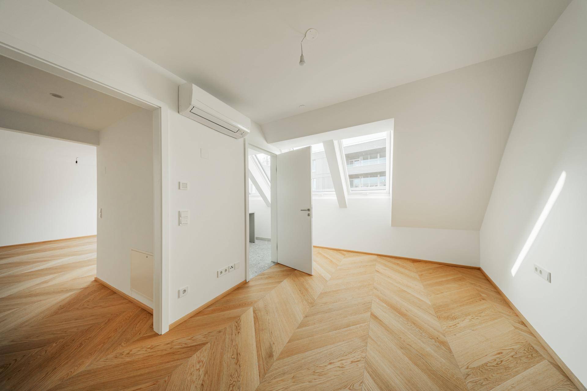 Geräumiges Zimmer mit schrägem Dachfenster, Fischgrätparkett und Klimaanlage.
