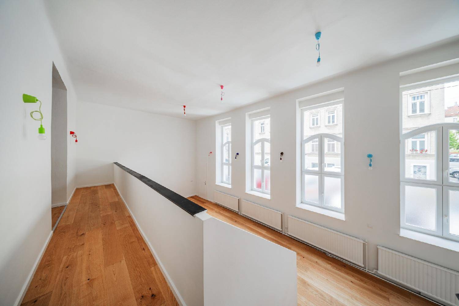 Heller Wohnraum mit Holzboden, hohen Fenstern und einer Galerie, die den Raum optisch erweitert.