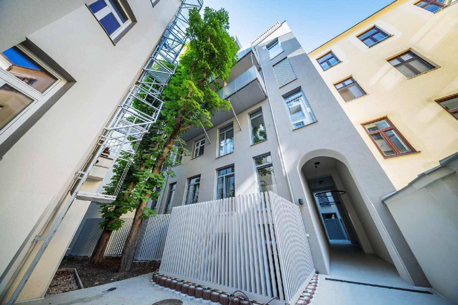 Blick in einen begrünten Innenhof mit hohen Bäumen und modernen Gebäudefassaden.