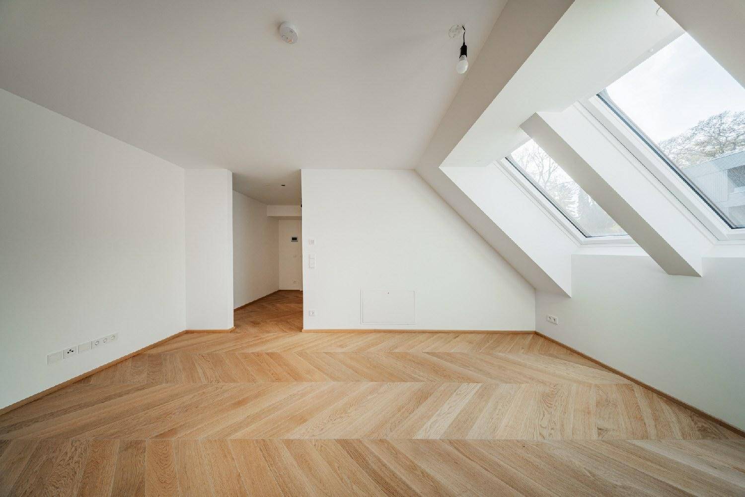 Heller Raum mit schrägen Dachfenstern und elegantem Fischgrätparkett, bietet viel natürliches Licht.