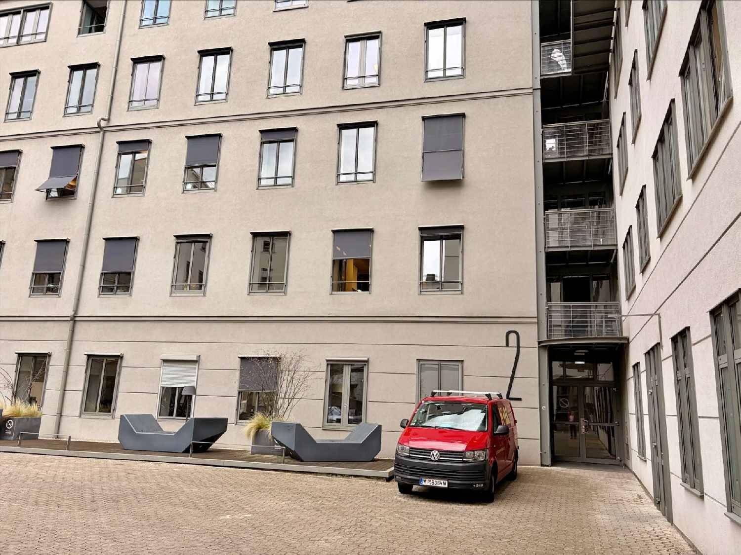 Eingangsbereich eines modernen Gebäudes mit Sitzgelegenheiten und einem roten Lieferwagen.