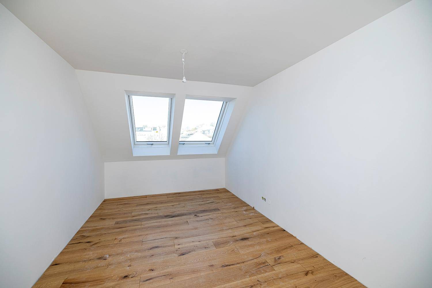 Helles Zimmer im Dachgeschoss mit Holzboden und schrägen Wänden, bereit zur Einrichtung.