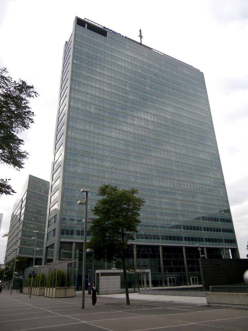Hohes Bürogebäude mit durchgehender Glasfassade und klarem Design unter bewölktem Himmel.