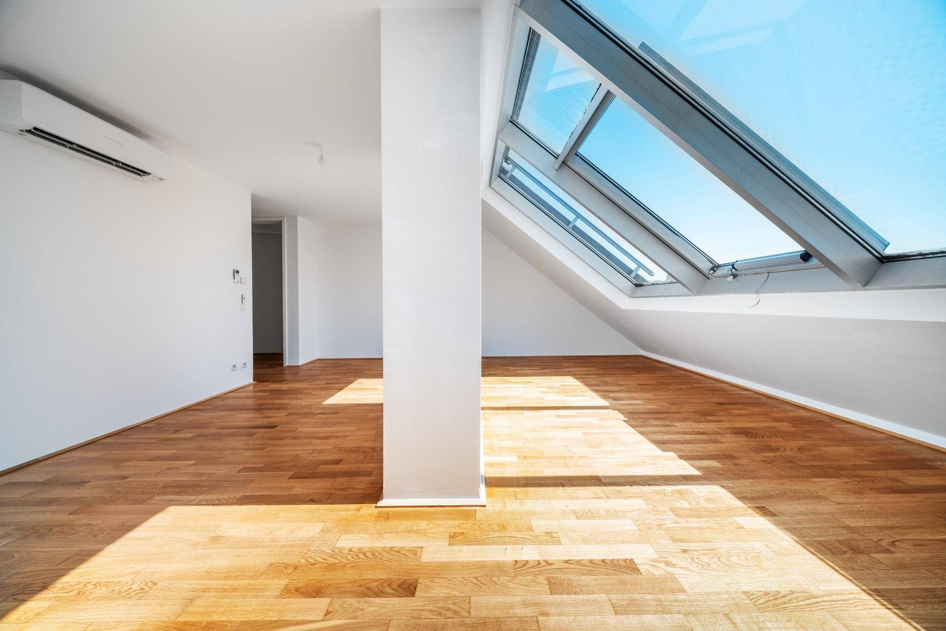 Heller Raum mit Holzboden, Klimaanlage und großen Dachfenstern, die den Raum lichtdurchfluten.