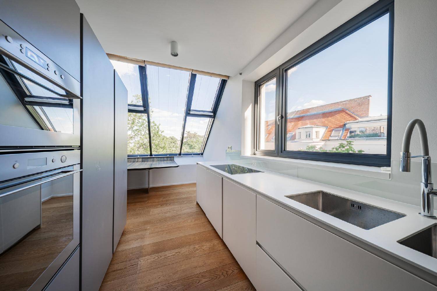 Moderne Küche mit weißen Schränken, integrierten Geräten und großen Fenstern mit Blick ins Grüne.