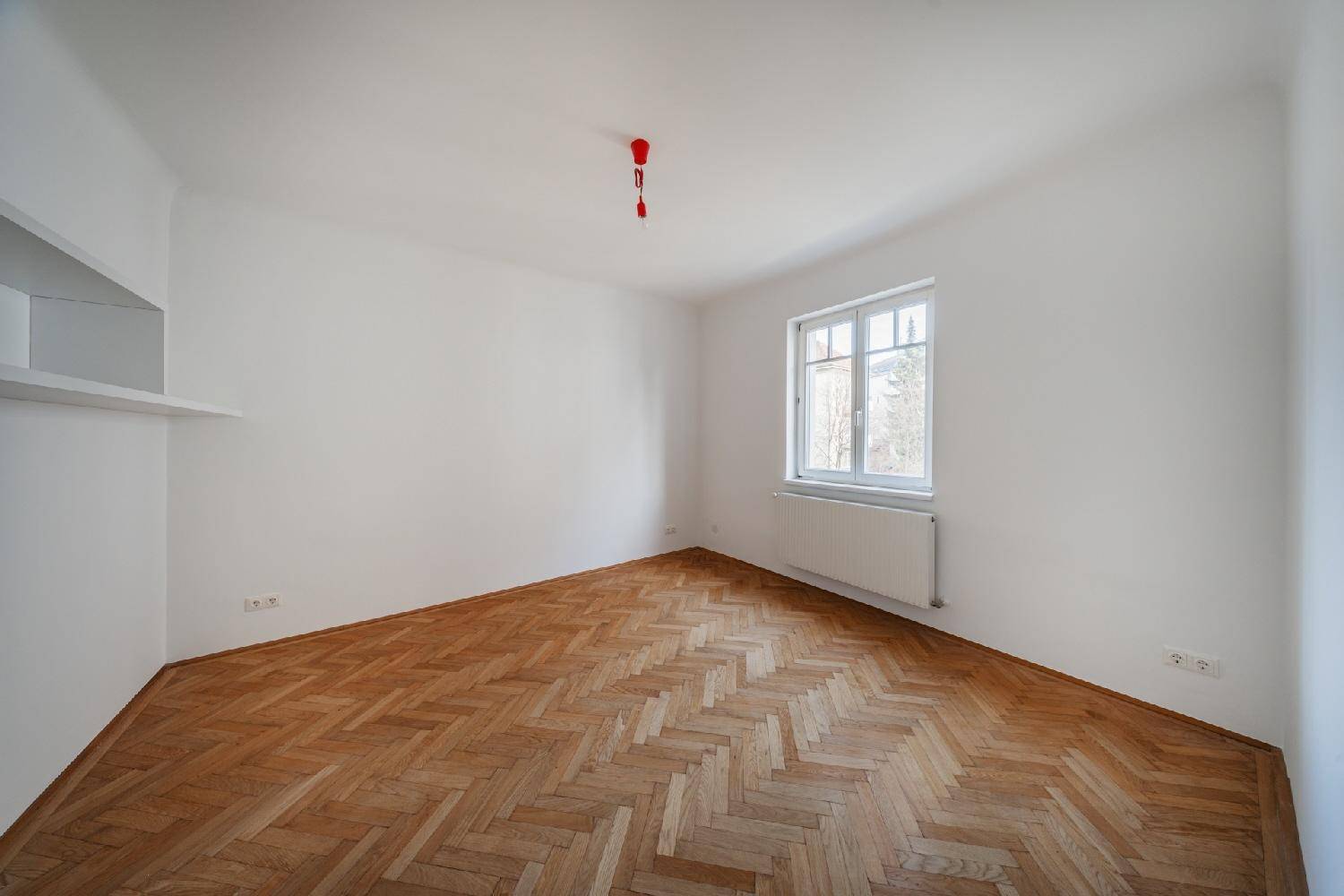 Helles Schlafzimmer mit Fischgrätparkett, neutralen Wänden und einem Fenster für natürliches Licht.