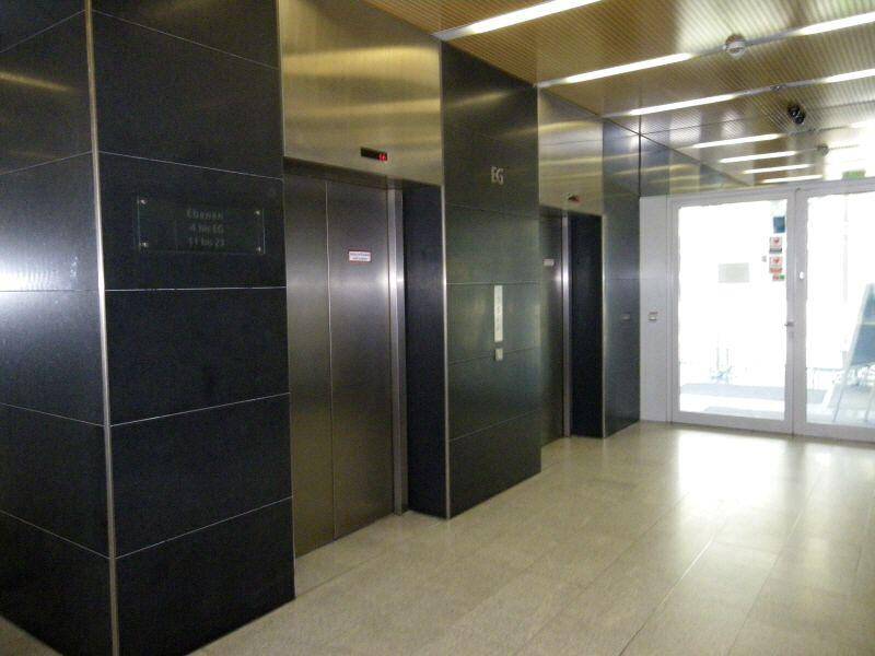 Moderner Aufzugsbereich mit dunklen Fliesen und glänzenden Metalltüren, gut beleuchtet und gepflegt.
