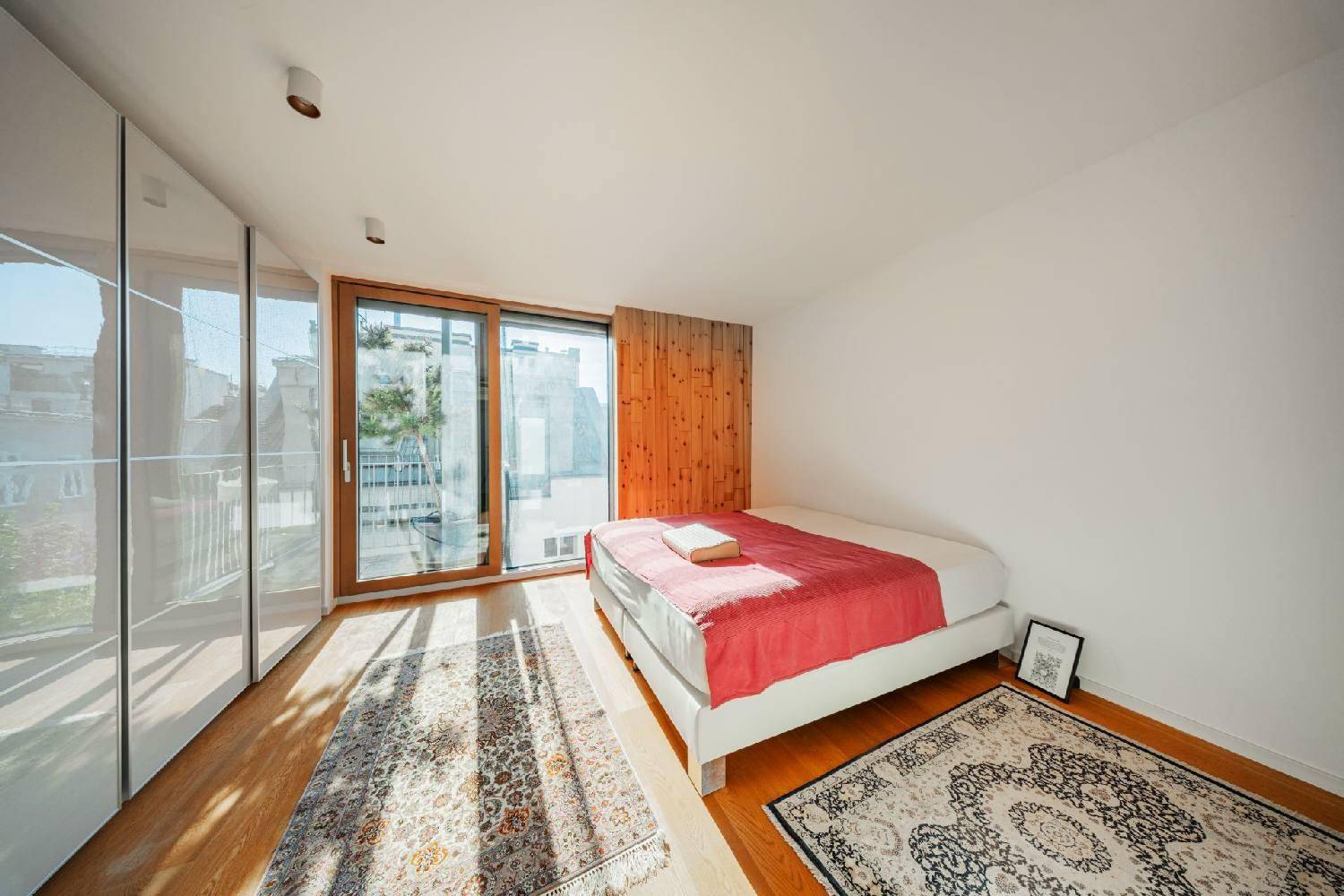 Sonniges Schlafzimmer mit Holzboden, Doppelbett und Zugang zu einem Balkon.