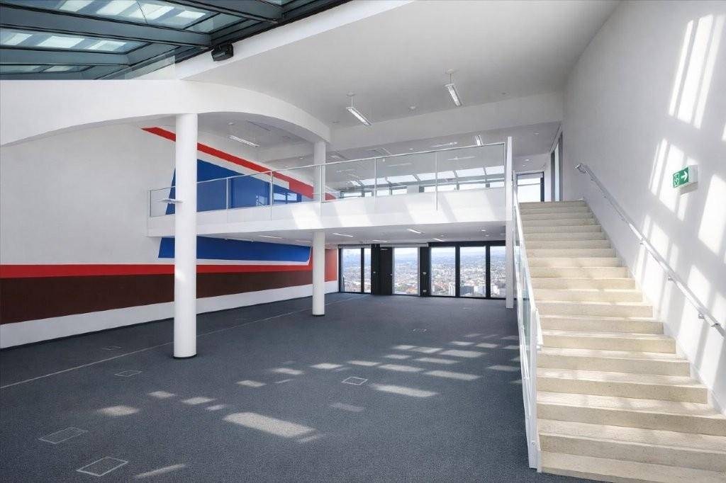 Moderner, offener Bürobereich über zwei Ebenen mit breiter Treppe, Glasgeländer und farbigen Akzentwänden.