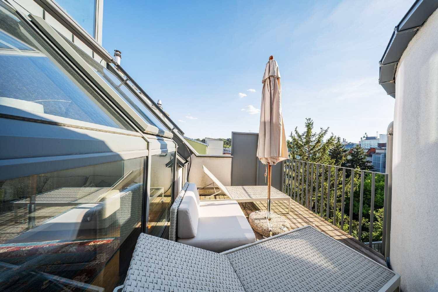 Kleiner Balkon mit Loungemöbeln und Blick auf die umliegenden Bäume und Dächer.