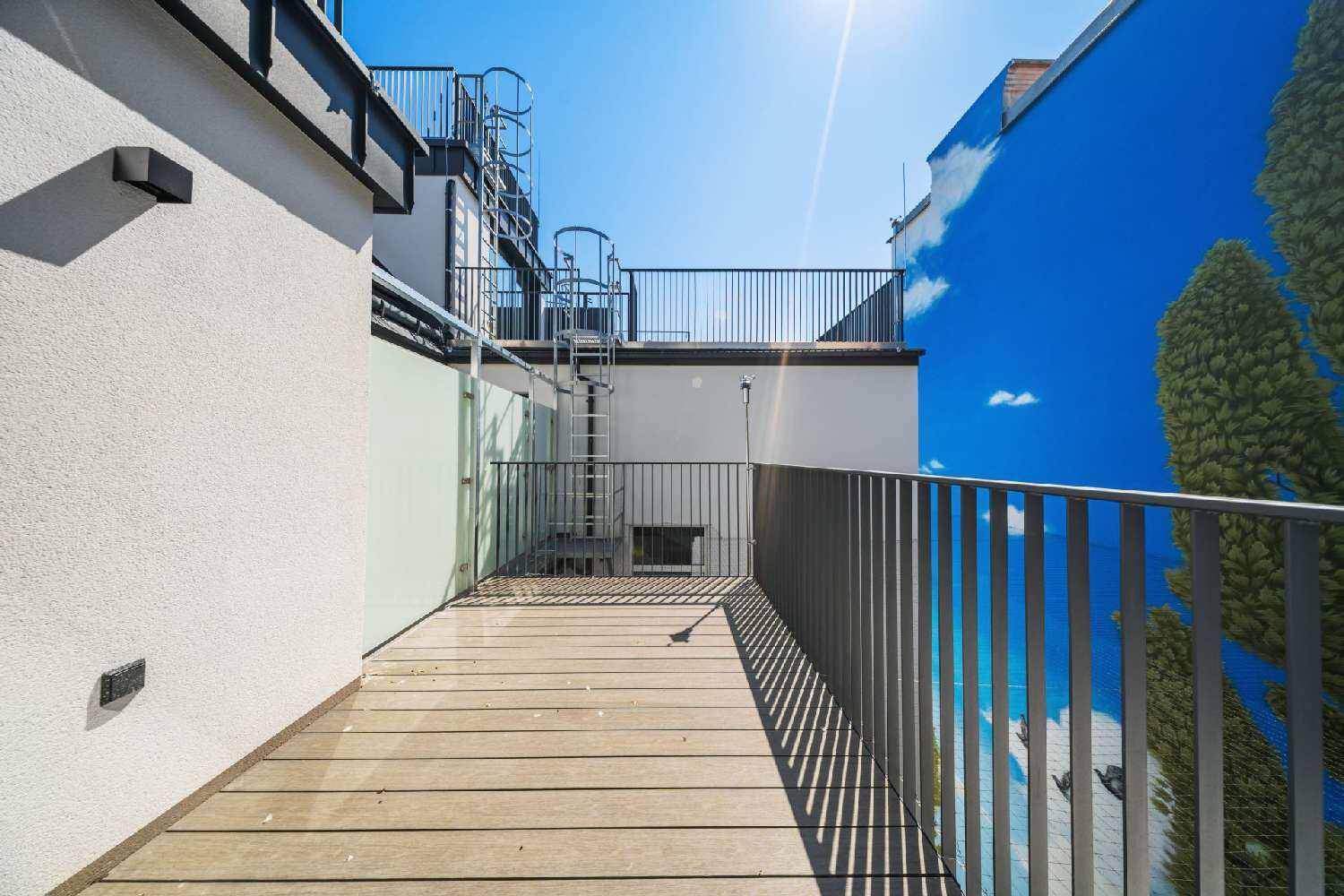 Sonnige Dachterrasse mit Holzbelag und Zugang zu einer weiteren Ebene über eine Wendeltreppe.