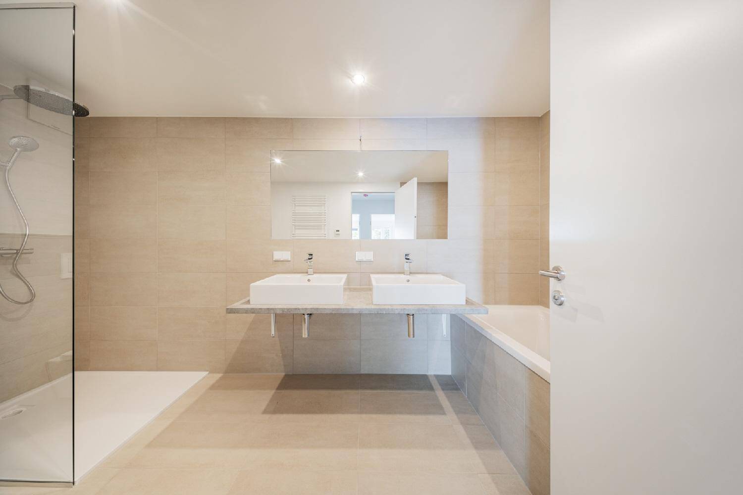 Modernes Badezimmer mit beigefarbenen Fliesen, Doppelwaschbecken, großer Dusche und Badewanne.