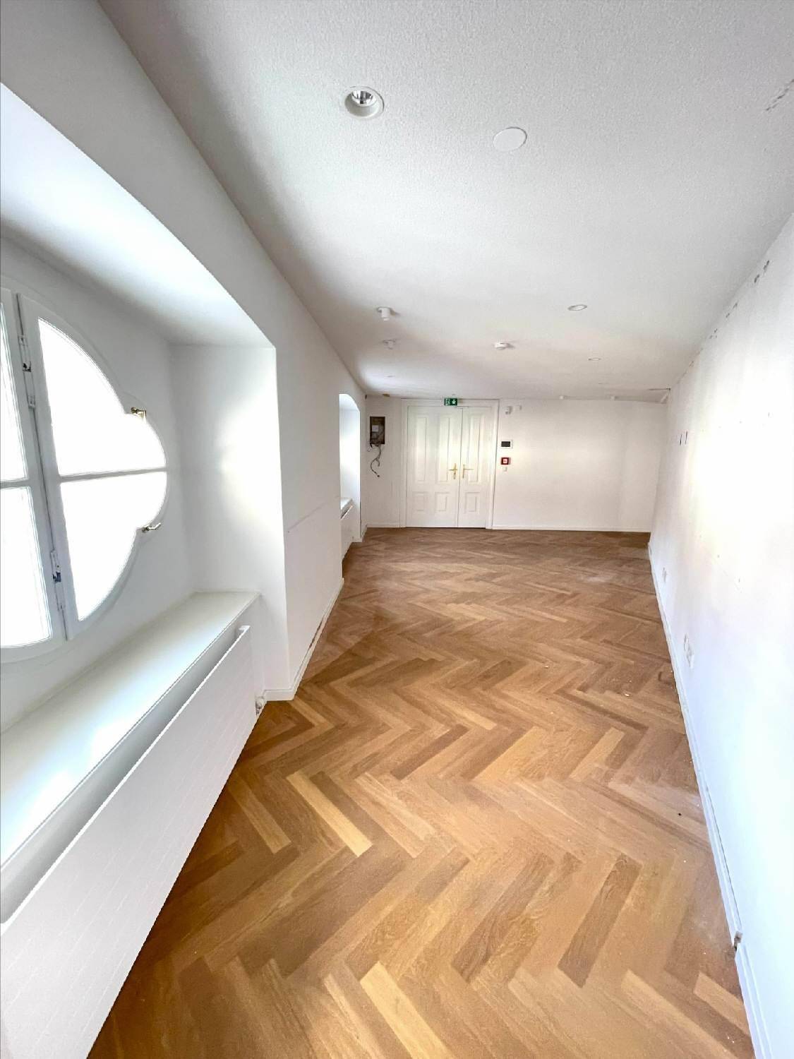 Heller Raum mit Fischgrätparkett und einem dekorativen Rundbogenfenster.