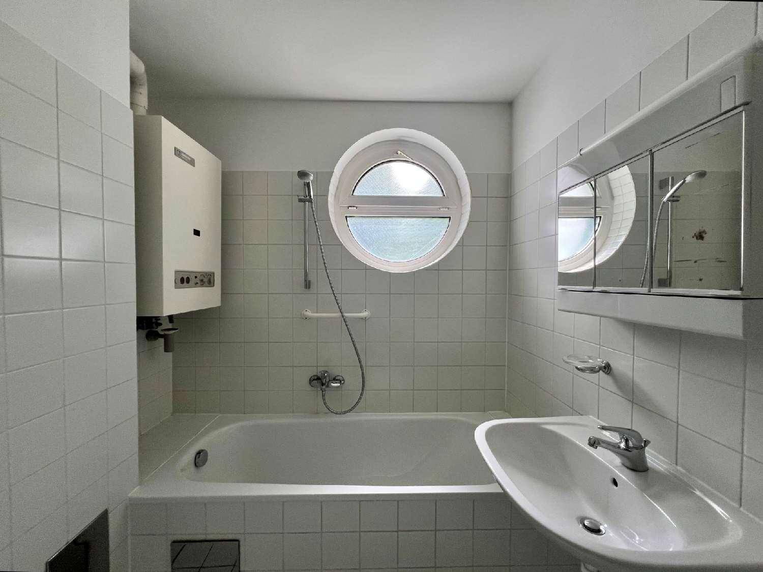 Badezimmer mit Badewanne, Waschbecken, Spiegelschrank und einem markanten runden Fenster.