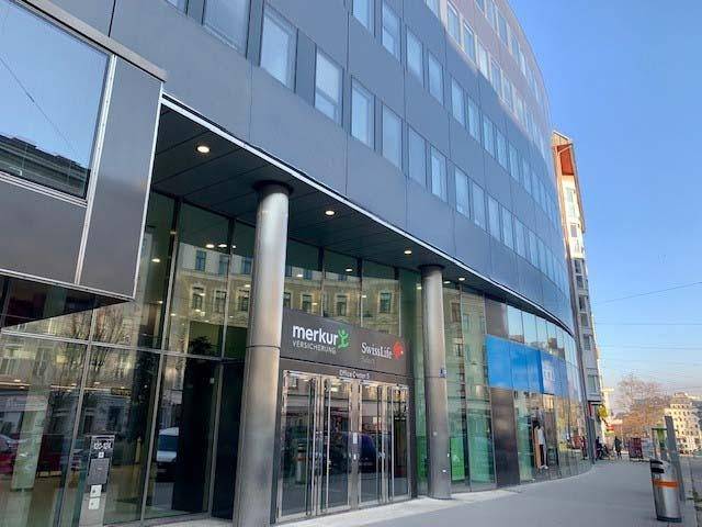 Eingangsbereich eines modernen Bürogebäudes mit Glasfassade und Firmenlogos an einem sonnigen Tag.