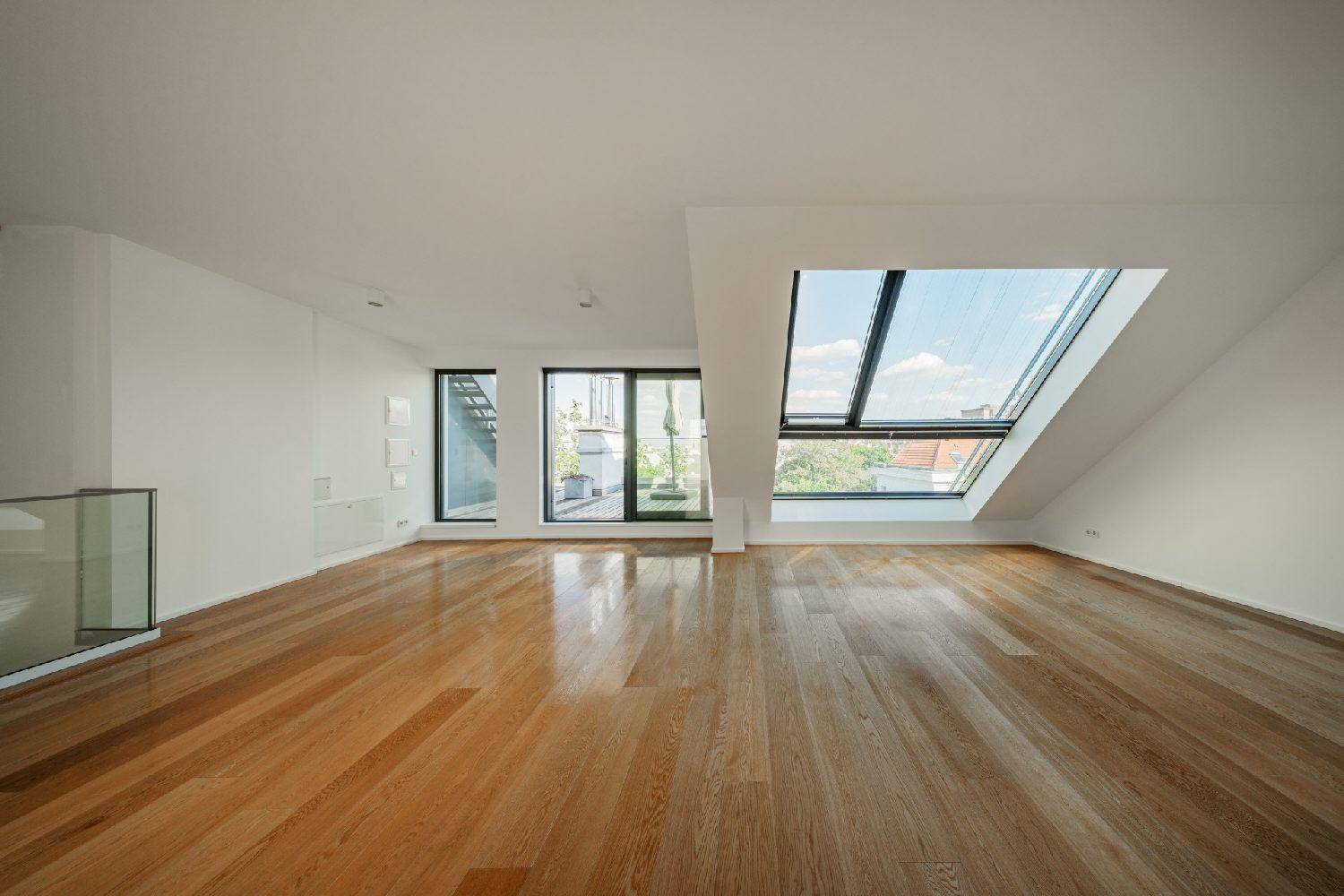 Heller Wohnraum mit Holzboden und großen Dachfenstern, die den Raum mit Sonnenlicht durchfluten.