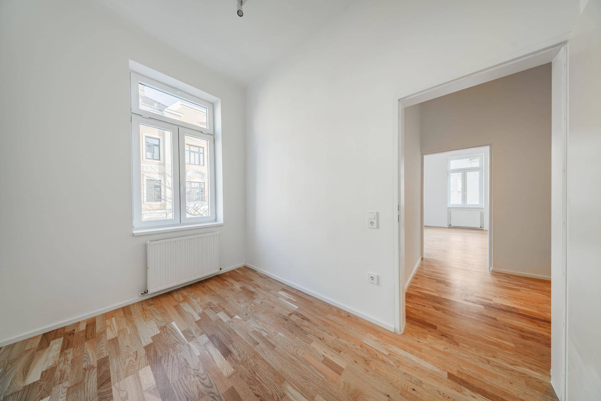 Leeres Zimmer mit Parkettboden und einem Fenster, das den Blick nach draußen freigibt.