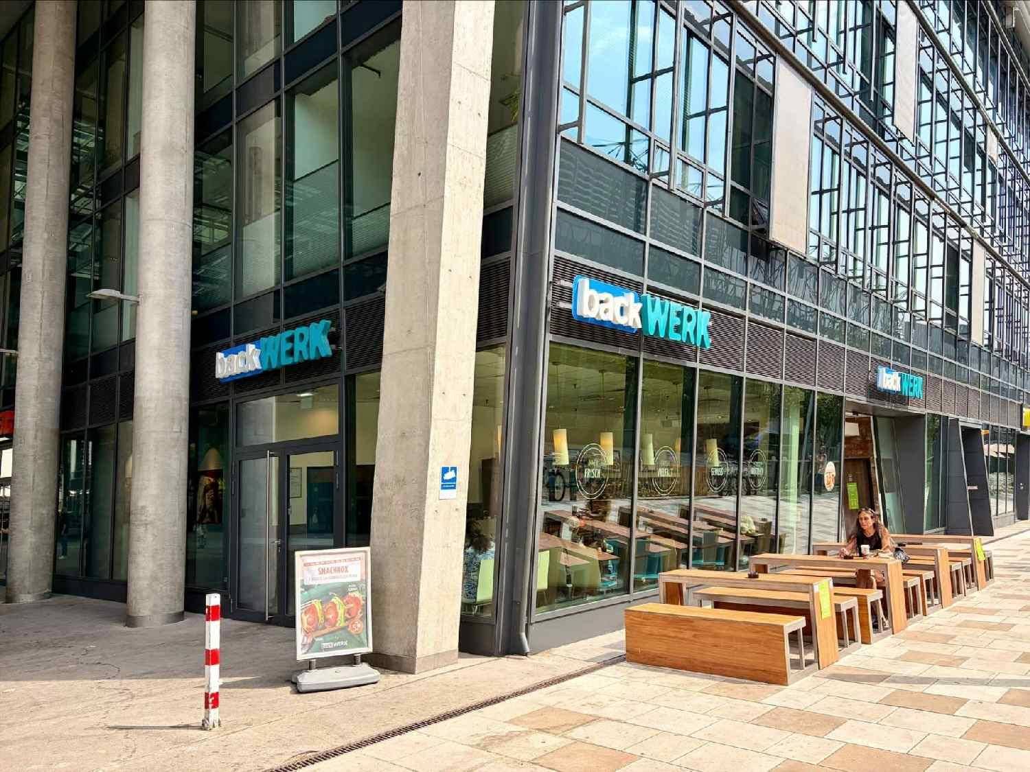 Außenansicht eines modernen Geschäftsgebäudes mit Glasfassade und Sitzgelegenheiten im Freien.