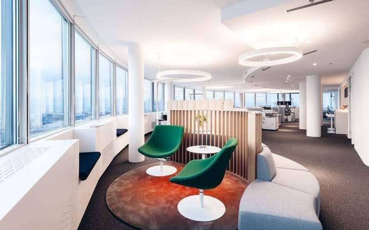 Gemütliche Sitzecke in einem modernen Büro mit grünen Stühlen, Teppich und Panoramablick auf die Stadt.