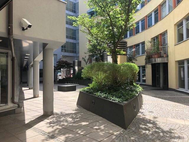 Sonniger Innenhof mit gepflastertem Bereich, begrünten Pflanzbeeten und moderner Gebäudearchitektur, lädt zum Verweilen ein.