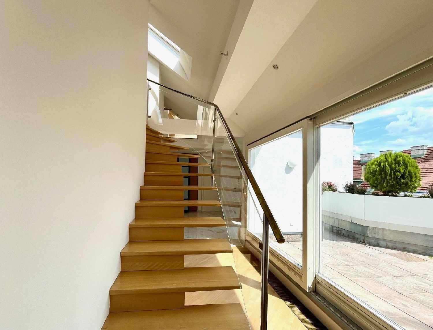 Elegante Holztreppe mit Glasgeländer, führt zu den oberen Etagen und bietet Zugang zur Terrasse.