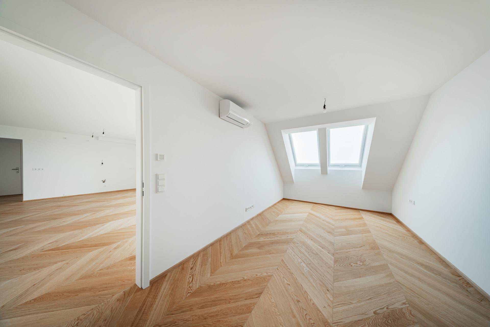 Gemütliches Schlafzimmer im Dachgeschoss mit schrägen Wänden, Dachfenstern und Fischgrätparkett.
