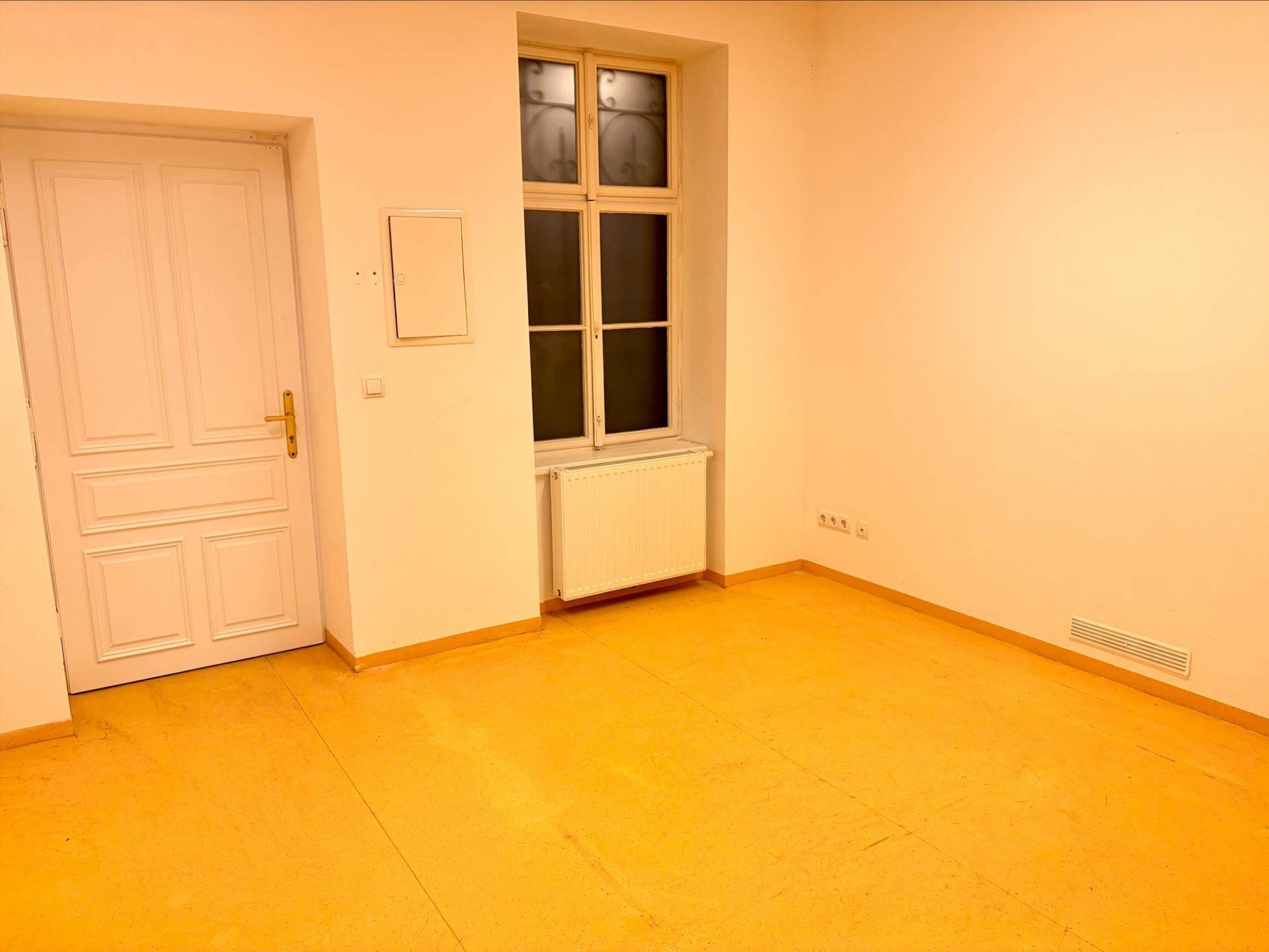 Heller Raum mit einem Fenster, einer weißen Tür und einem Heizkörper unter dem Fenster.