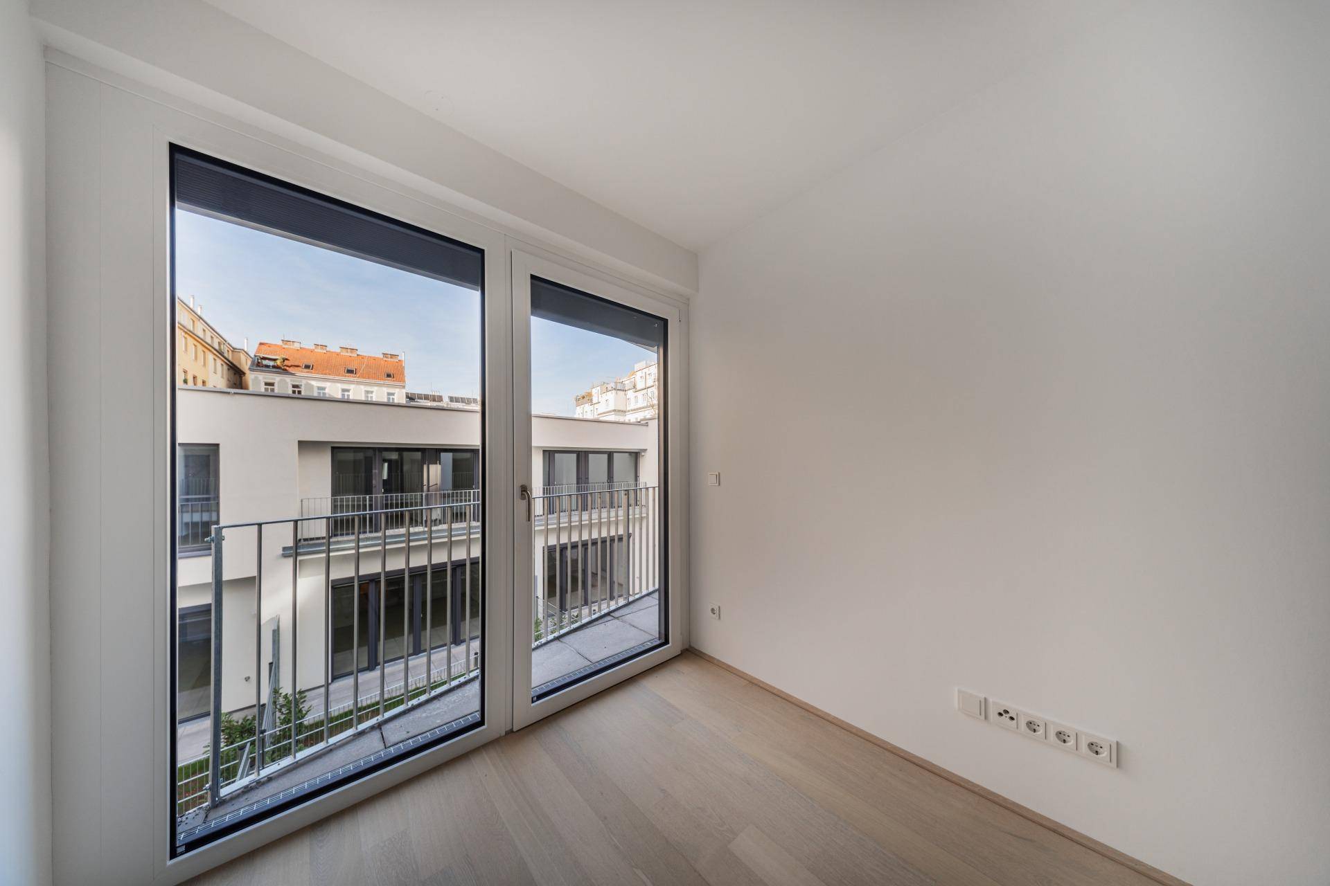 Lichtdurchflutetes Zimmer mit Parkettboden und großem Fenster mit Blick auf den Innenhof.