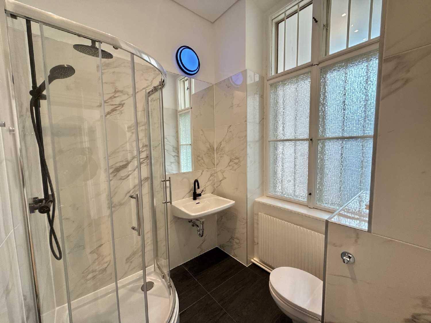 Modernes Badezimmer mit Duschkabine, wandhängendem WC, Einzelwaschbecken und eleganten Marmorfliesen.