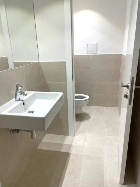 Modernes Badezimmer mit Waschbecken, Spiegel und Wand-WC, ausgestattet mit hellen Fliesen.