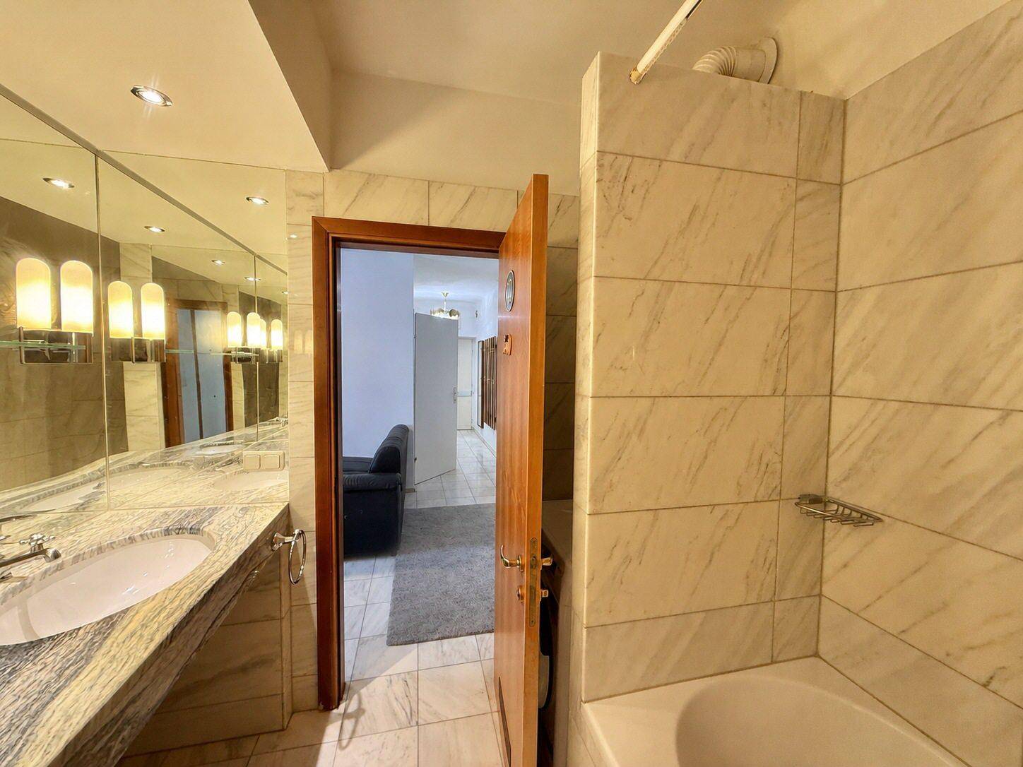 Elegantes Badezimmer mit Marmorwaschtisch, großem Spiegel und Zugang zu einem weiteren Raum.