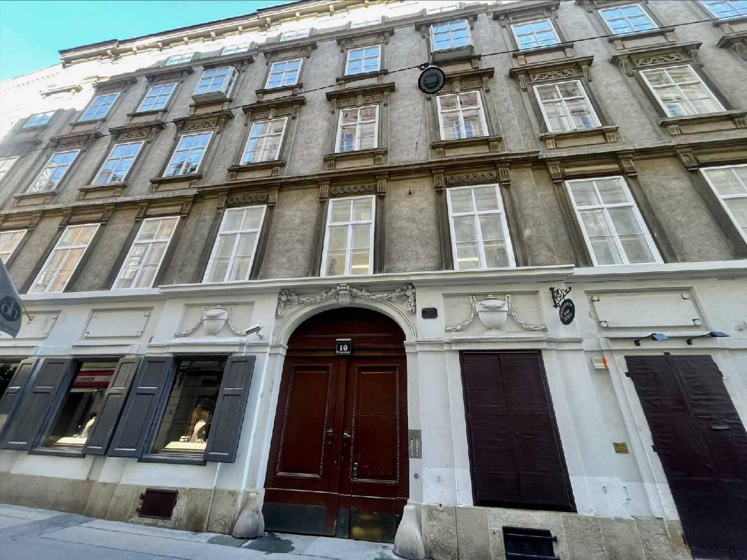 Historische Fassade eines Mehrfamilienhauses mit vielen Fenstern und einem großen Holztor im Erdgeschoss.